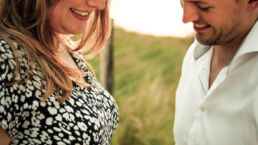 Zwangerschap fotoshoot vrouw en man in duinen met handen op buik