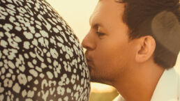 Zwangerschap fotoshoot man kust buik van vrouw voor tegenlicht