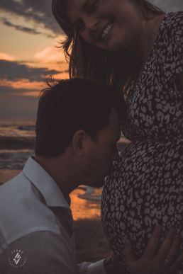 Zwangerschap fotoshoot man kust buik van vrouw voor ondergaande zon in de zee