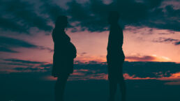 Zwangerschap fotoshoot man en vrouw in silhouet voor gekleurde lucht na zonsondergang